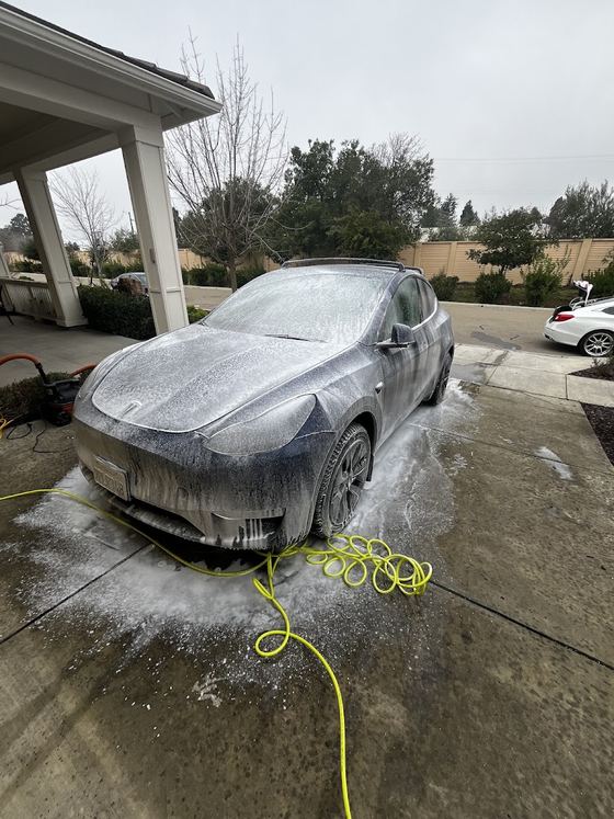 A Tesla covered in snow foam on a driveway during a Gordos Suds detail